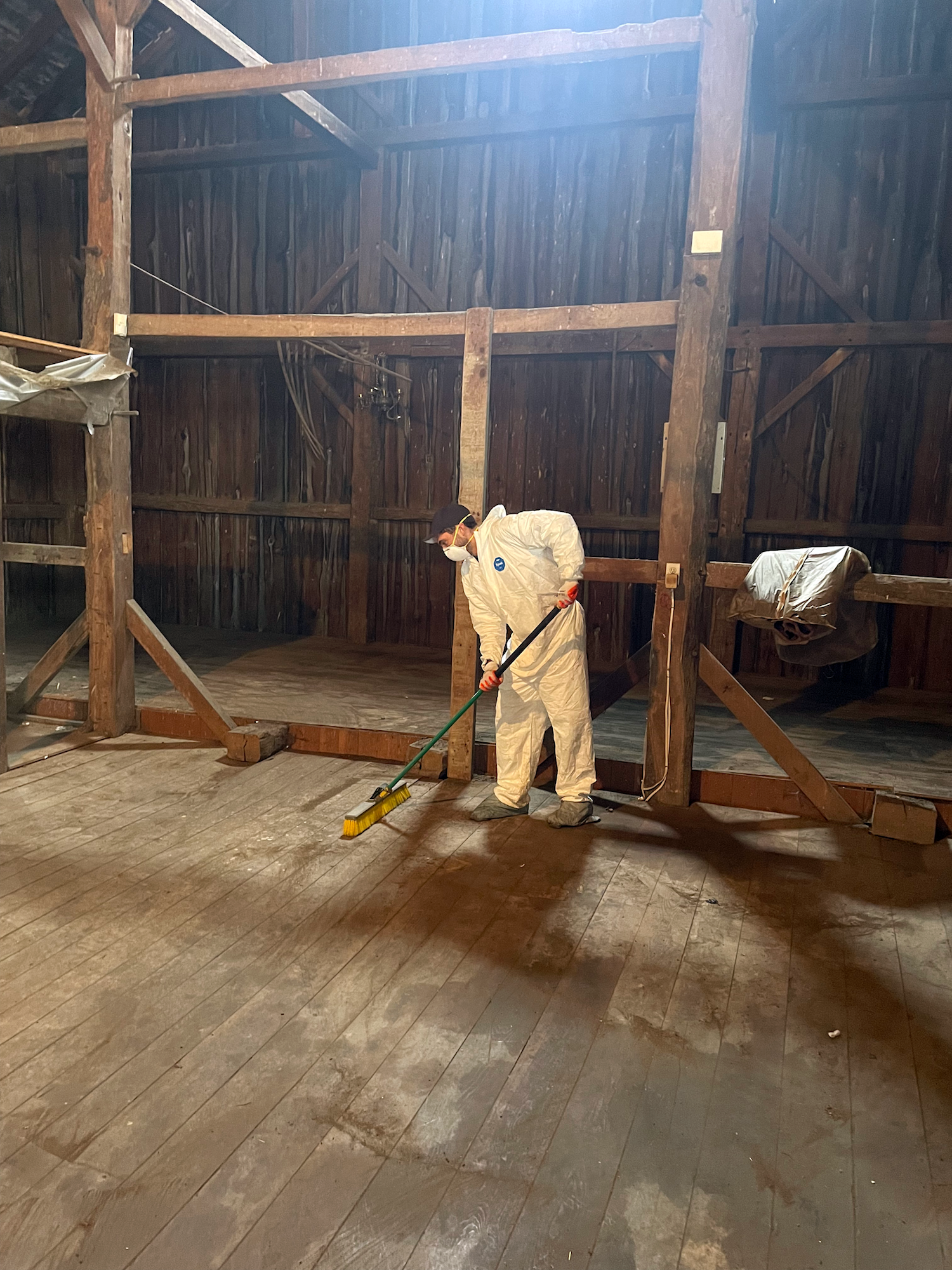 employee sweeping a dusty barn